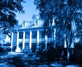 A blue and white photo of a large house surrounded by trees