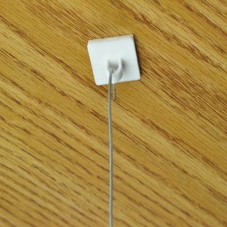 Clip adhesivo blanco sobre una superficie de madera que sujeta un alambre fino y plateado.