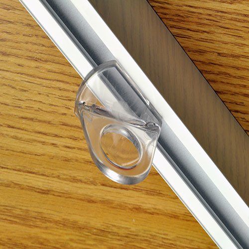 Gancho para cortina en forma de anillo de plástico transparente sujeto a un riel plateado sobre una superficie de madera.