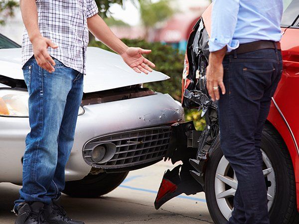 Two men at car accident scene, inspecting damage to silver and red vehicles.