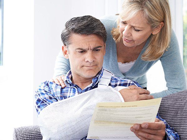 Man with arm in sling looking at document, woman comforting him.