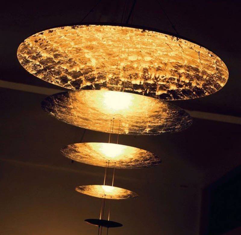 Quattro lampade a sospensione circolari dorate pendono da un soffitto scuro e irradiano una luce calda.