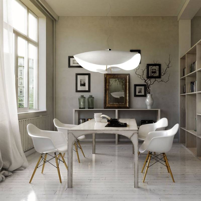 Sala da pranzo con tavolo bianco, sedie e grande lampada a sospensione. Una finestra lascia entrare la luce.