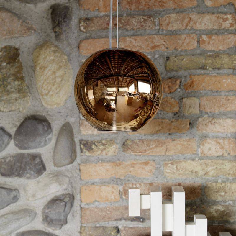 Lampada a sospensione a sfera in rame su muro di mattoni e pietra.