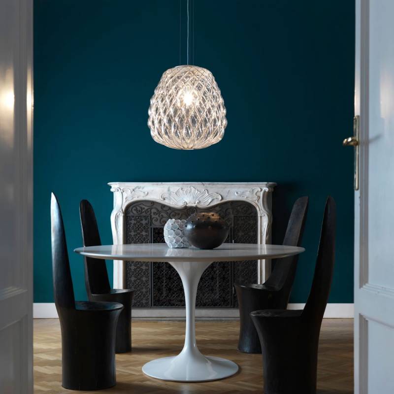 Sala da pranzo con tavolo rotondo, sedie nere, camino decorato e lampada a sospensione testurizzata. Parete color verde acqua.