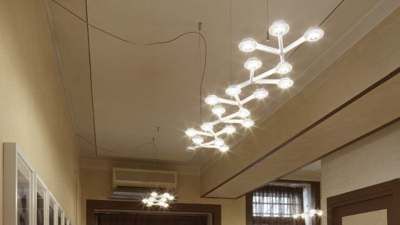 Una moderna lampada bianca a bracci illumina un corridoio con soffitto e pareti chiare.