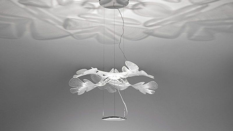 Un moderno lampadario a forma di fiore pende, proiettando ombre a motivi sul soffitto bianco.