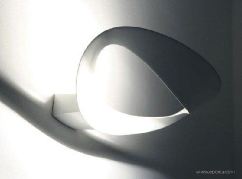 Scultura astratta in carta bianca che proietta ombre su una superficie bianca.