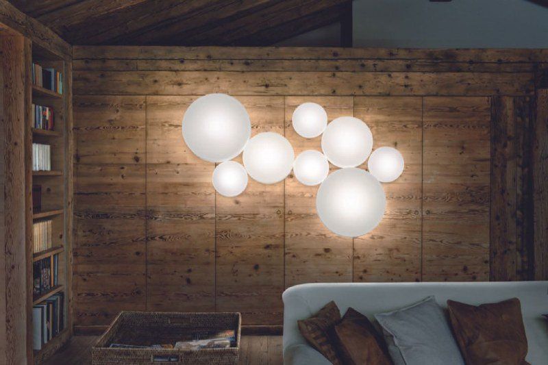 Luci a bolla montate su una parete rivestita in legno, che illuminano uno spazio abitativo con divano e libreria.
