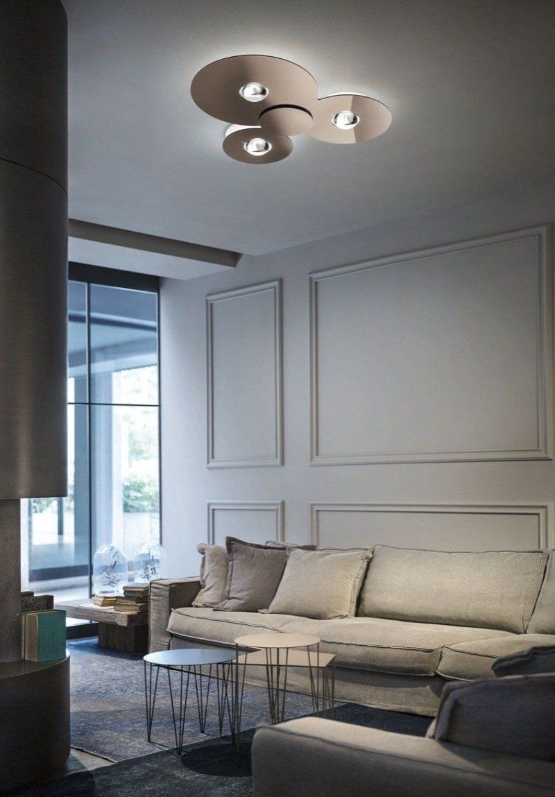 Soggiorno con divano beige, modanature alle pareti e lampadario moderno a soffitto.