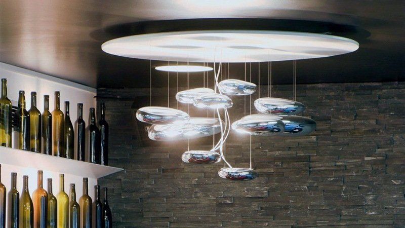Lampadario moderno con numerose luci ovali riflettenti e fluttuanti appese a un elemento circolare del soffitto.