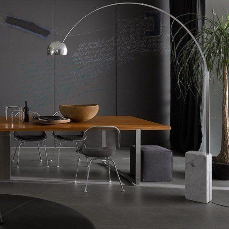 Lampada da terra ad arco sopra un tavolo da pranzo con sedie, una ciotola di legno e una base di marmo.