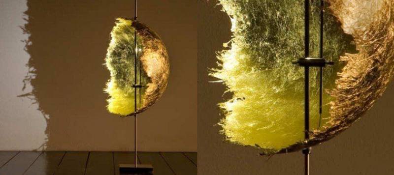 Una scultura simile al cotone, nei toni del giallo e del marrone, è appesa a un'asta di metallo.