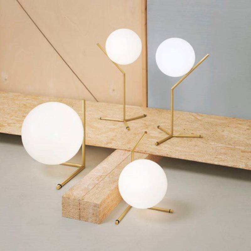Quattro lampade da tavolo in ottone con globi sferici in vetro bianco su una superficie in legno.
