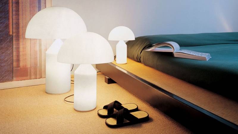 Lampade da tavolo bianche a forma di fungo di diverse dimensioni illuminano la stanza. Sono presenti anche un letto e delle pantofole.
