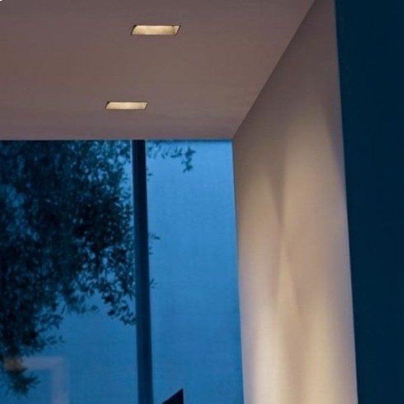 Le luci da incasso nel soffitto illuminano il soffitto bianco e la parete adiacente, con una vista esterna blu.