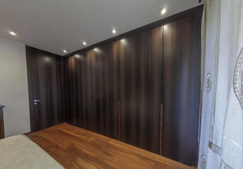 Armadio in legno scuro con illuminazione da incasso e pavimenti in legno in una camera da letto.