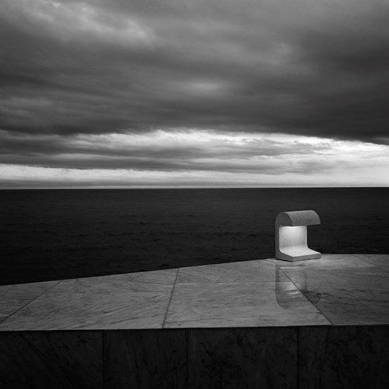 Una lampada moderna risplende su una superficie di marmo che domina un oceano scuro sotto un cielo tempestoso.