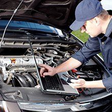 A man is working on the engine of a car with a laptop.