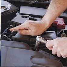 A person is working on a car engine with a wrench.