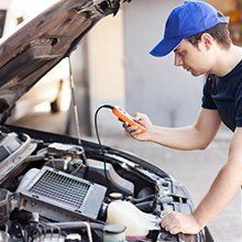 A man in a blue hat is working on the engine of a car.