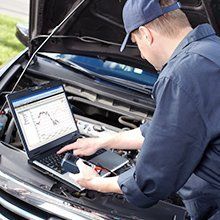 A man is using a laptop computer under the hood of a car.