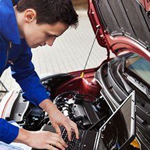 A man is working on a car engine with a laptop.