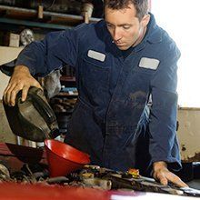 A man in a blue jumpsuit is pouring gas into a red bowl.
