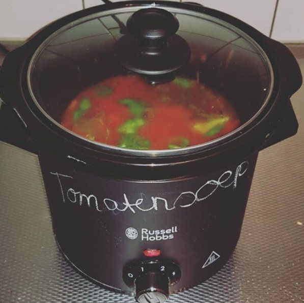 Een slowcooker met tomatensoep. Zwarte pot met de tekst 