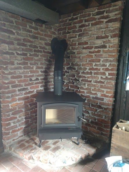Wood-burning stove in a brick corner. Black stove with chimney against a red brick wall and hearth.