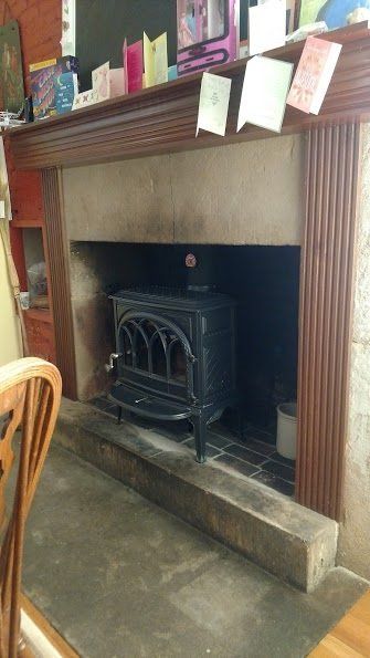 Black wood-burning stove inside a fireplace with a wood mantle and cards on top.