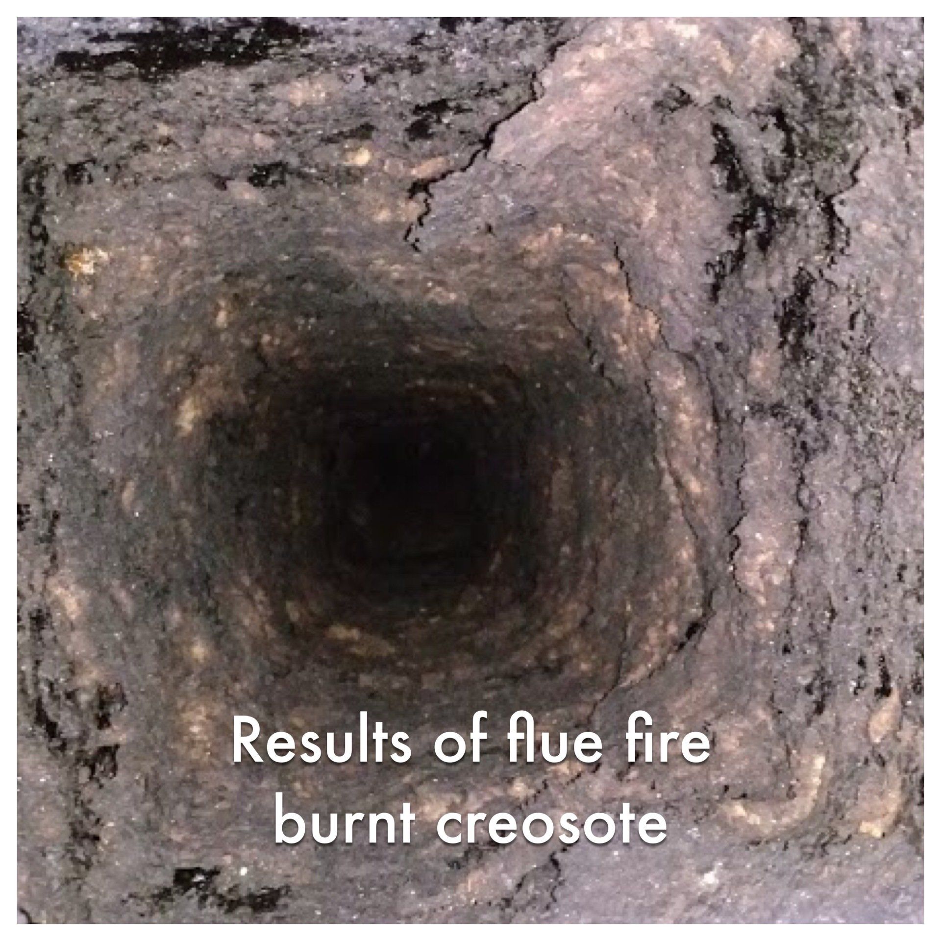 Looking down into a square chimney flue with thick, charred creosote buildup, the result of a flue fire.