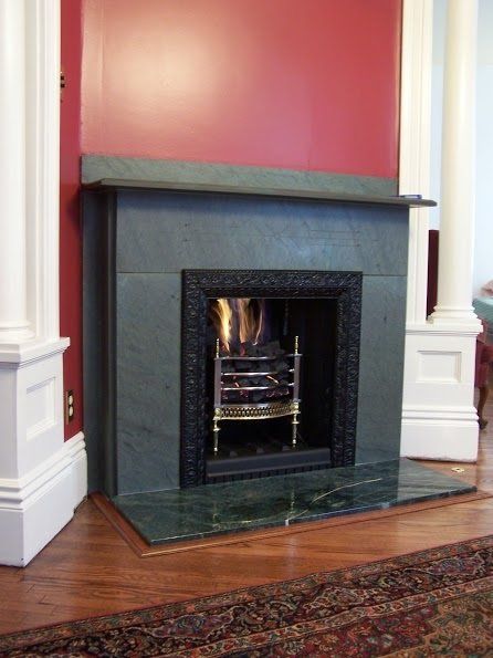 Green marble fireplace with a fire burning, set against a red wall.