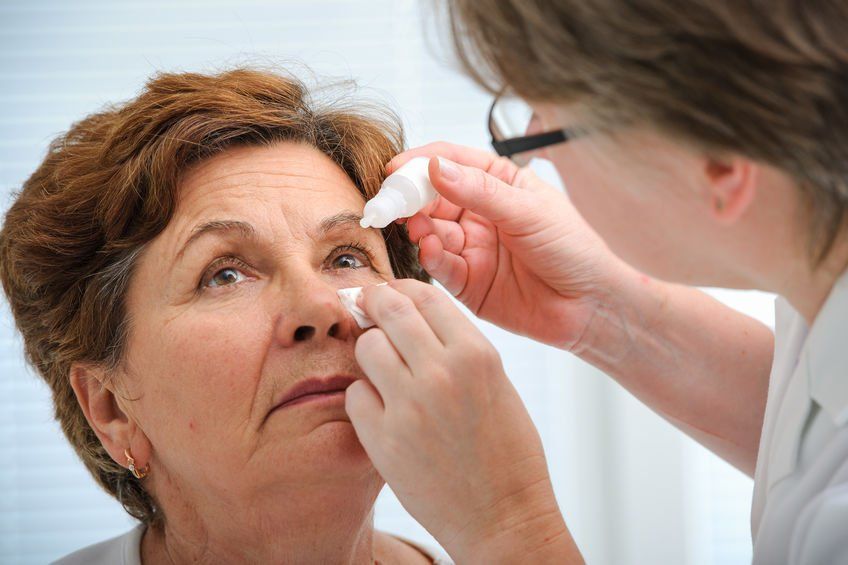 Optometrist adding eyedrops to female patients eyes.