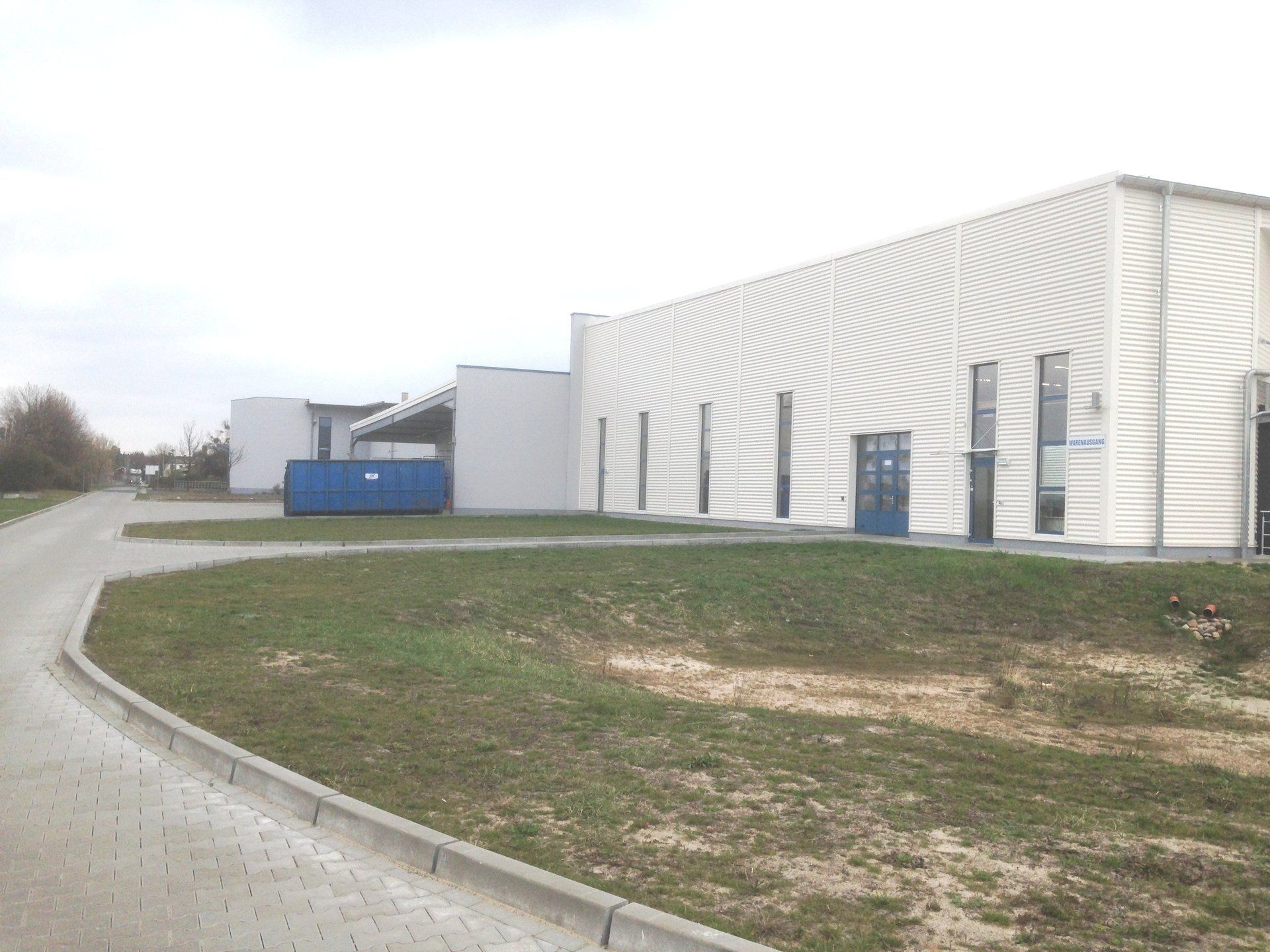 A large white building with a blue dumpster in front of it.