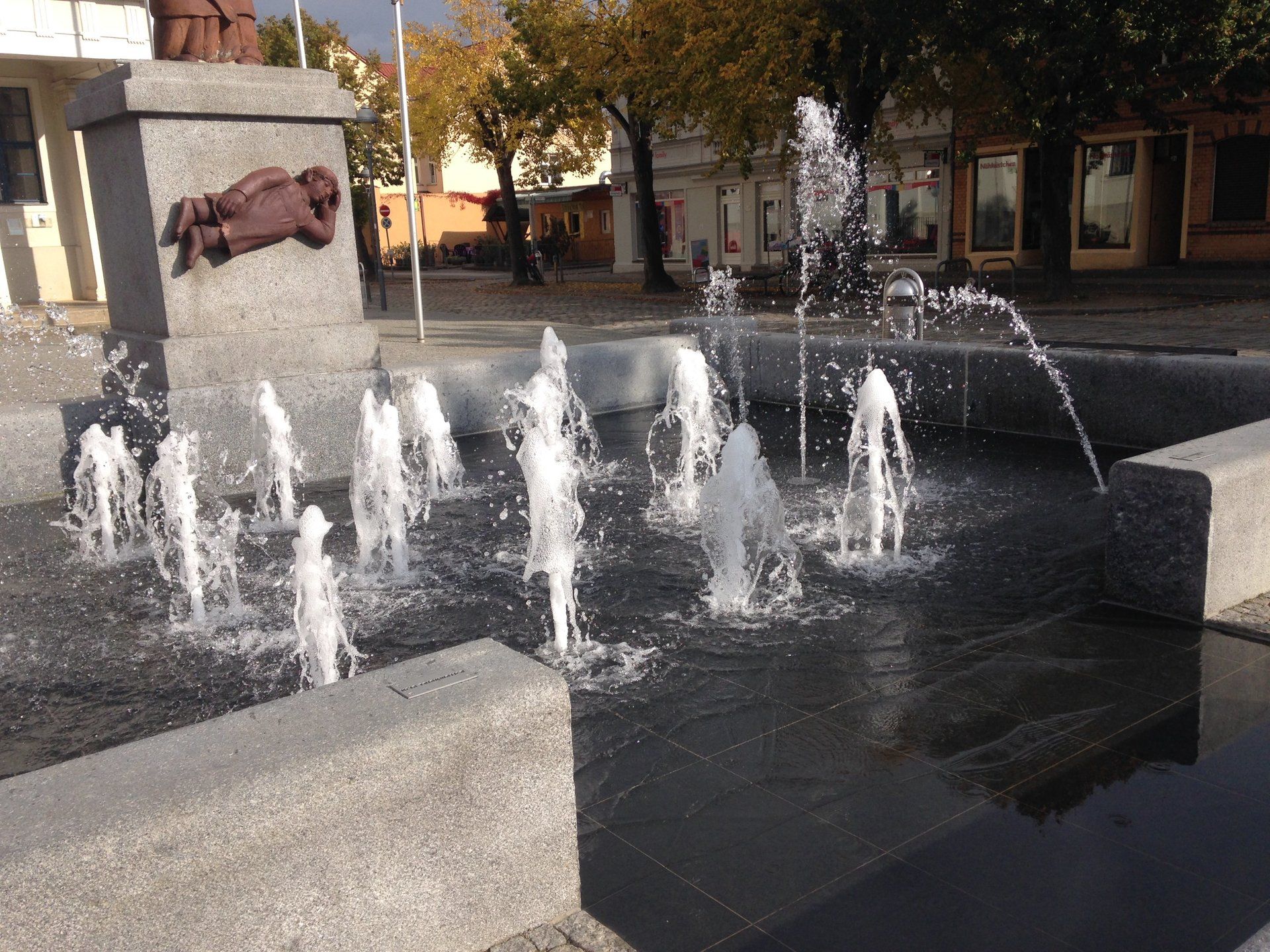 A fountain in a park with a statue in the background