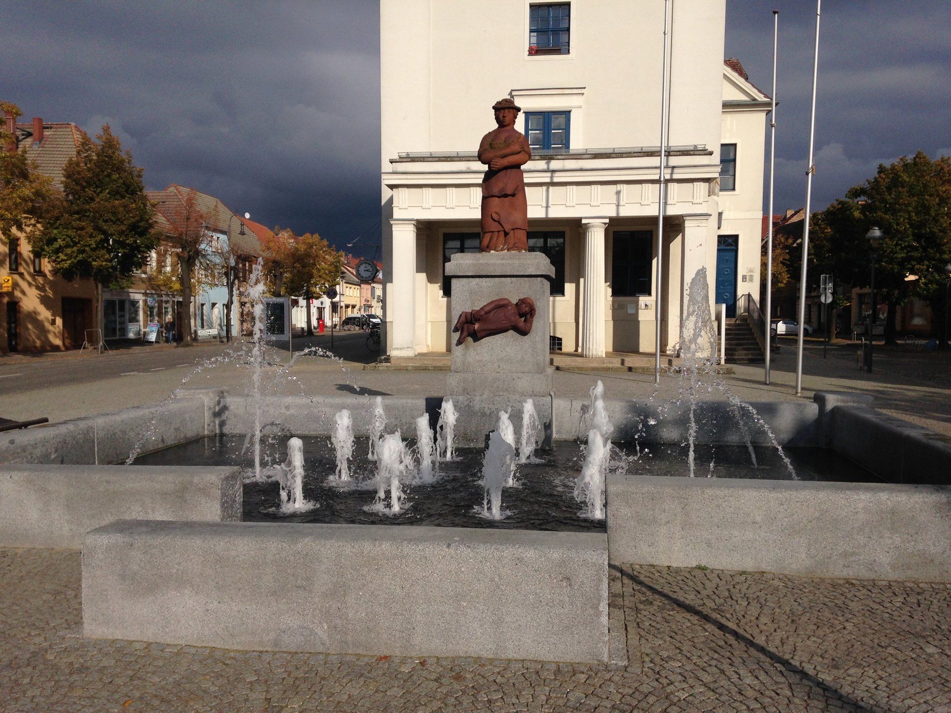 A fountain in front of a building with a statue in the background