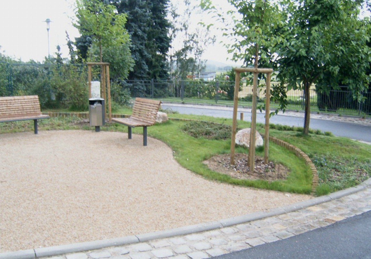 A park with two benches and trees on the side of the road