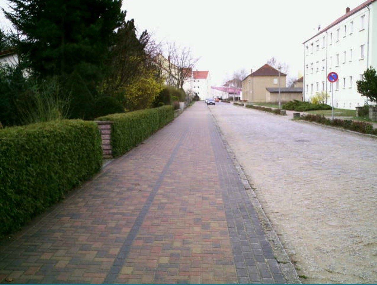 A brick walkway with a hedge on the side of it