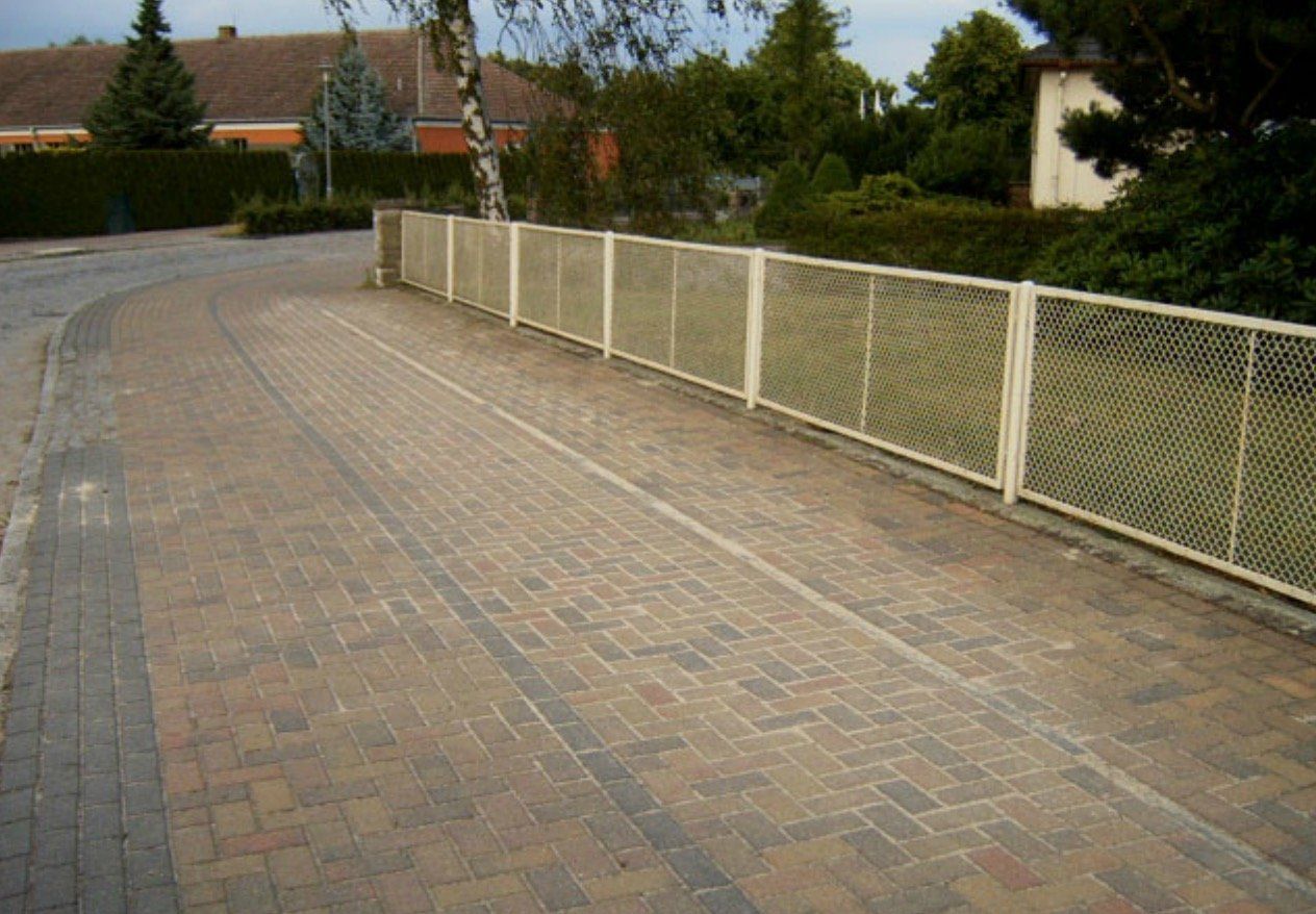 A brick walkway with a white fence along the side of it