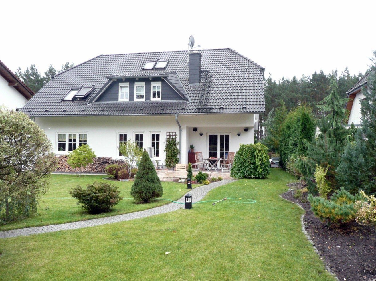 A large white house with a black roof sits in the middle of a lush green yard