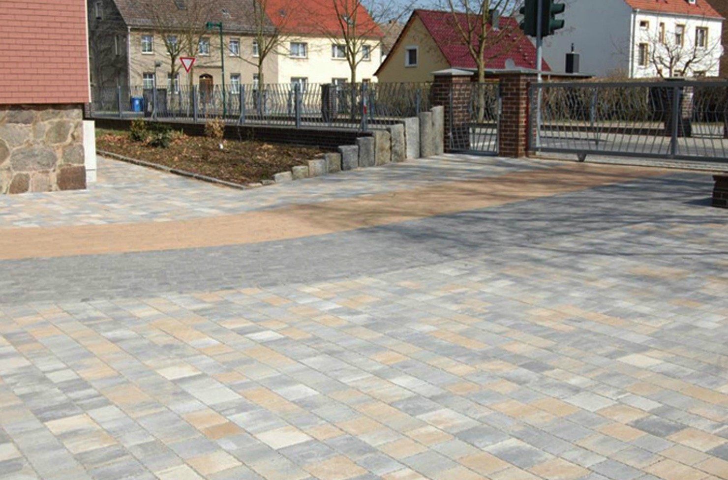 A brick driveway with a fence and houses in the background