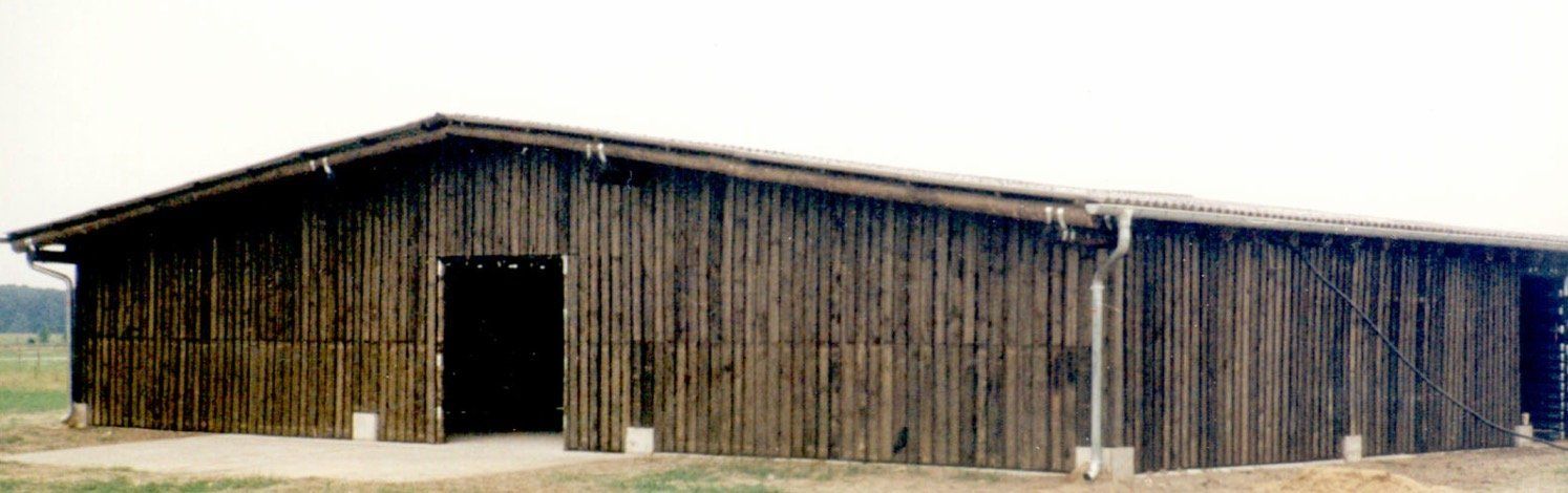 A large wooden barn is sitting in the middle of a field.