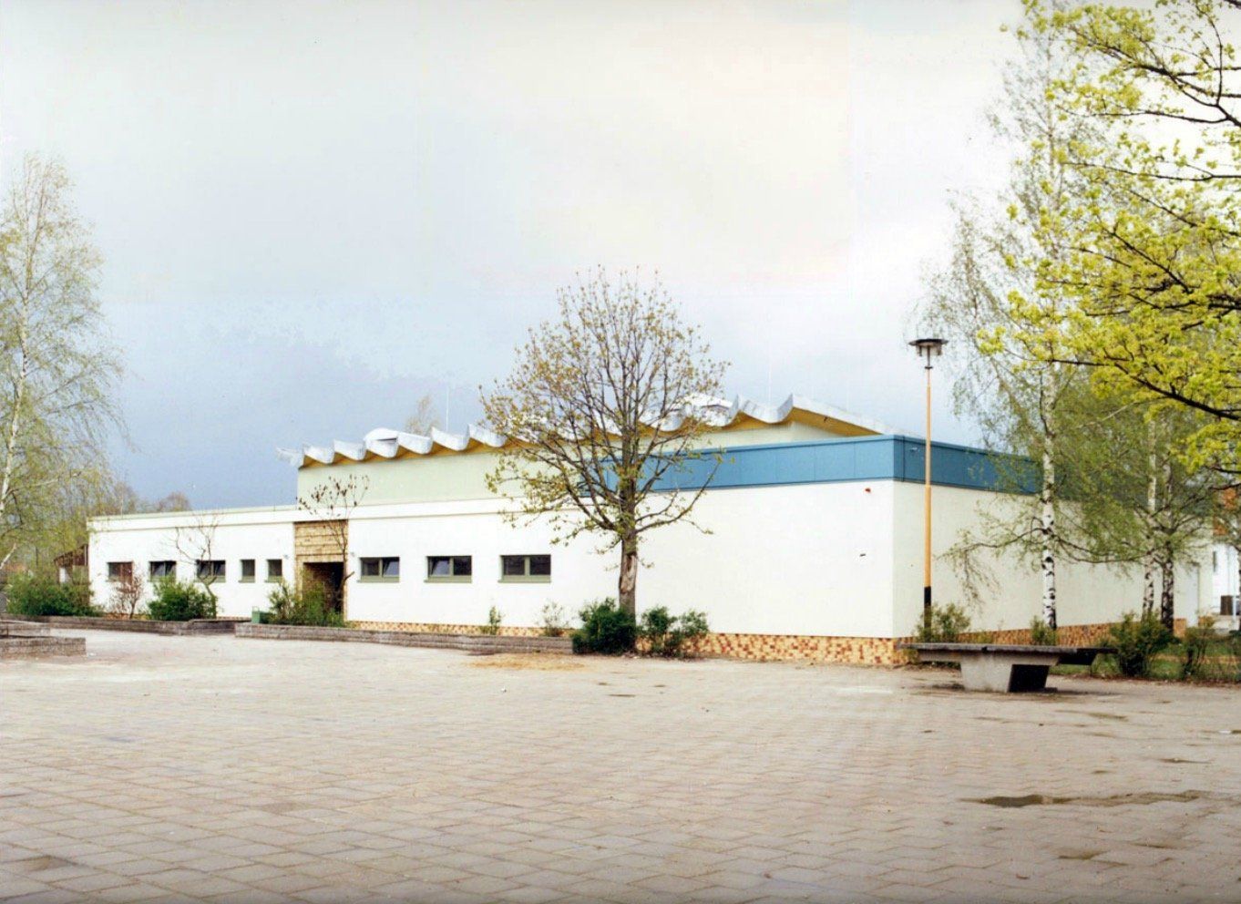 A large white building with a blue roof is surrounded by trees