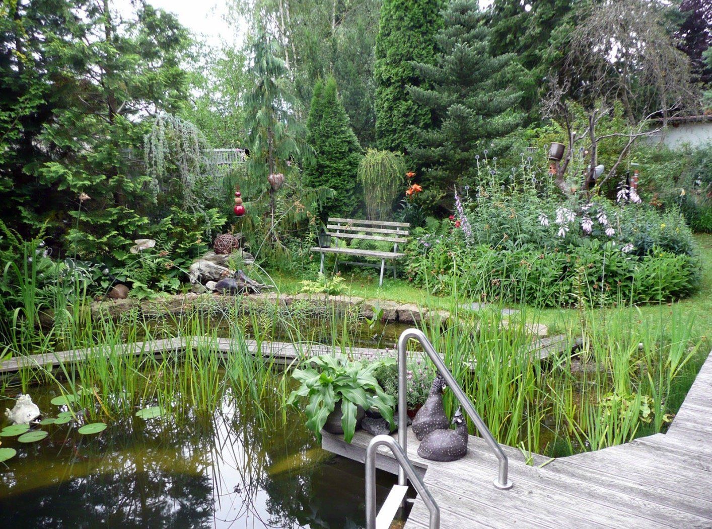There is a pond in the middle of a garden with a bench in the background.