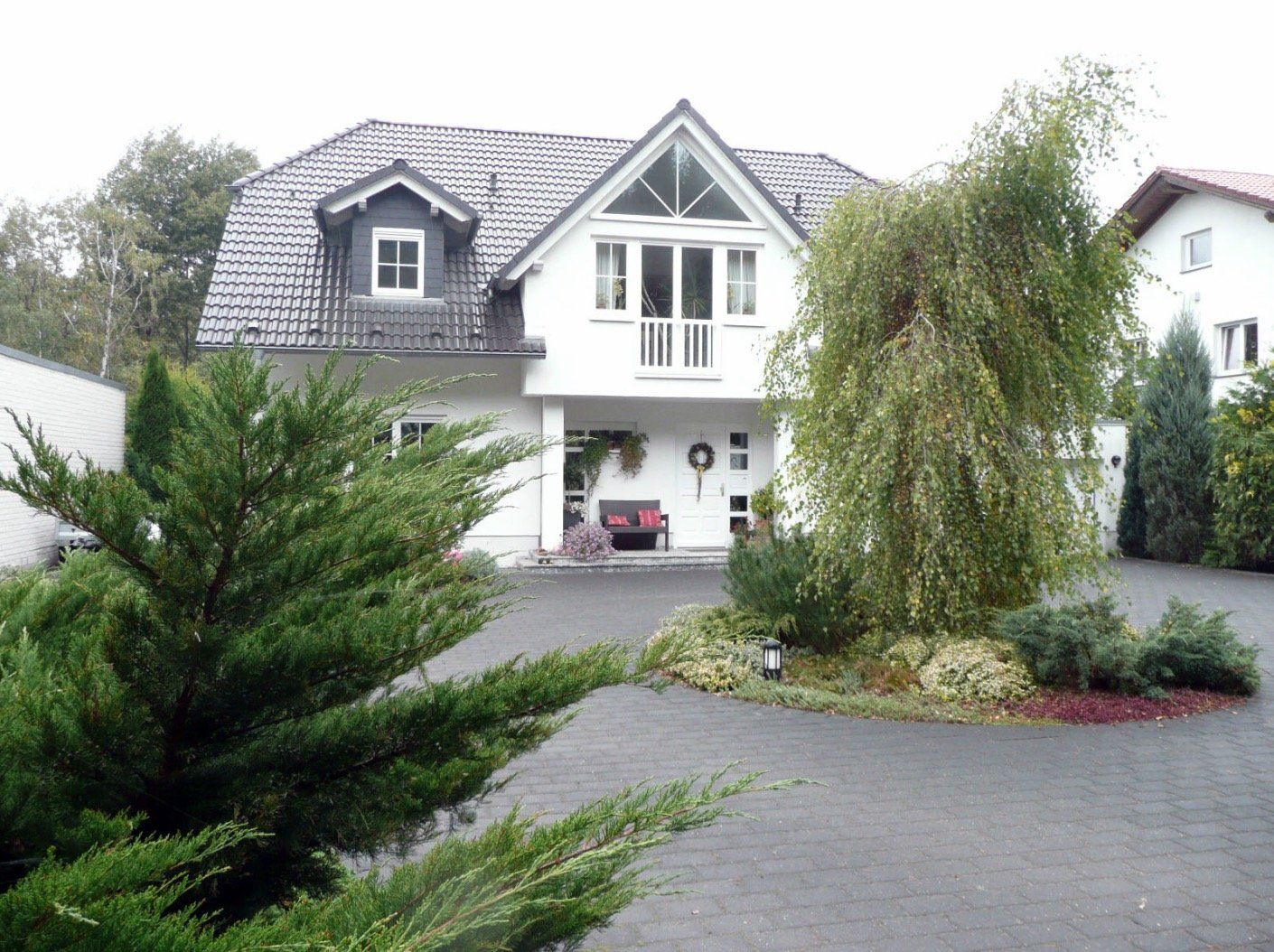 A large white house with a gray roof is surrounded by trees