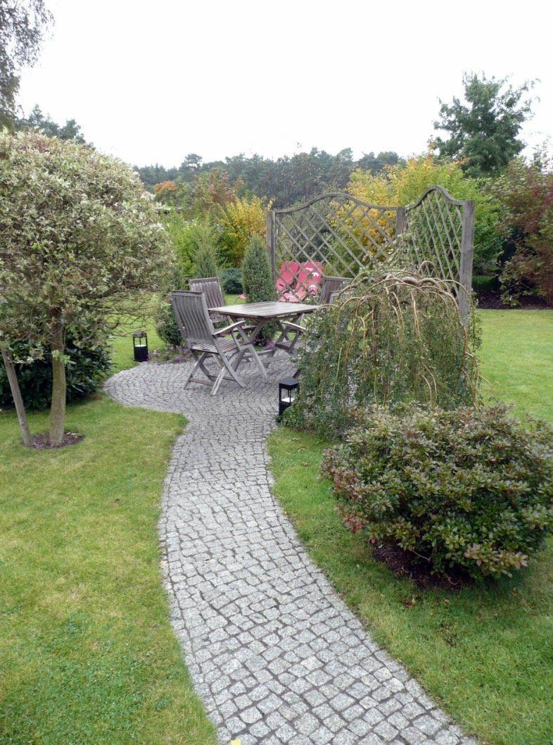 A cobblestone path leading to a table and chairs in a garden.