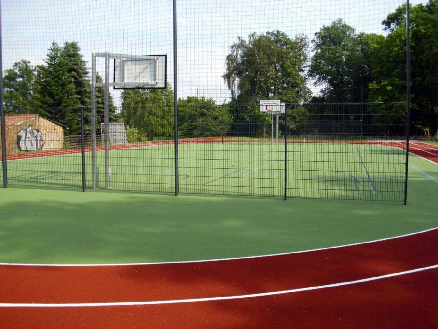 A basketball court with a fence around it and trees in the background