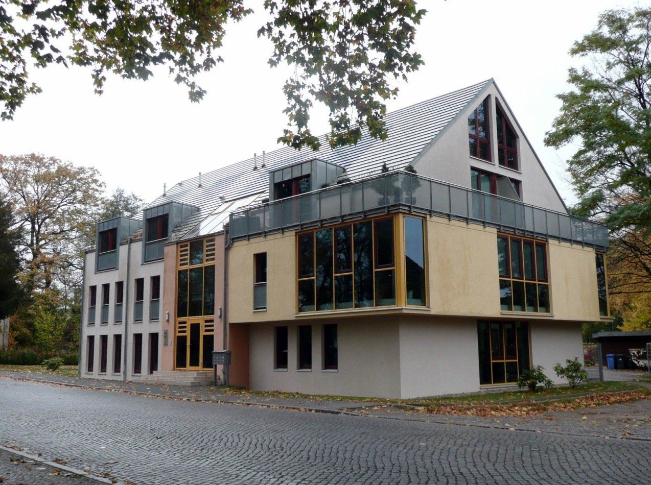 A large building with a lot of windows sits on a cobblestone street