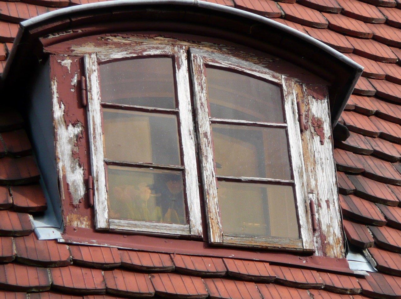 A window with peeling paint sits on top of a roof